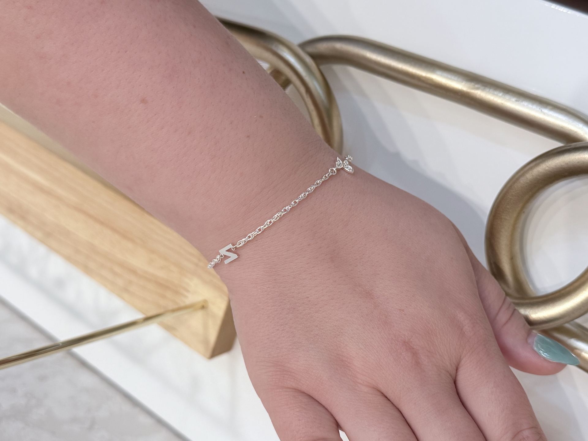 Silver bracelet with a small letter charm and a cluster of clear gemstone leaves, layered with a second silver chain